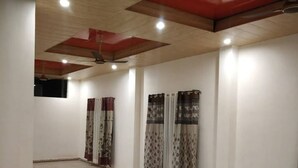 A spacious room with tiled flooring, a high ceiling with exposed beams, and a ceiling fan. - Hotel brijwasi palace (Yamkeshwar)