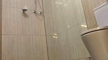 Un baño con ducha, paredes de azulejos y un inodoro.