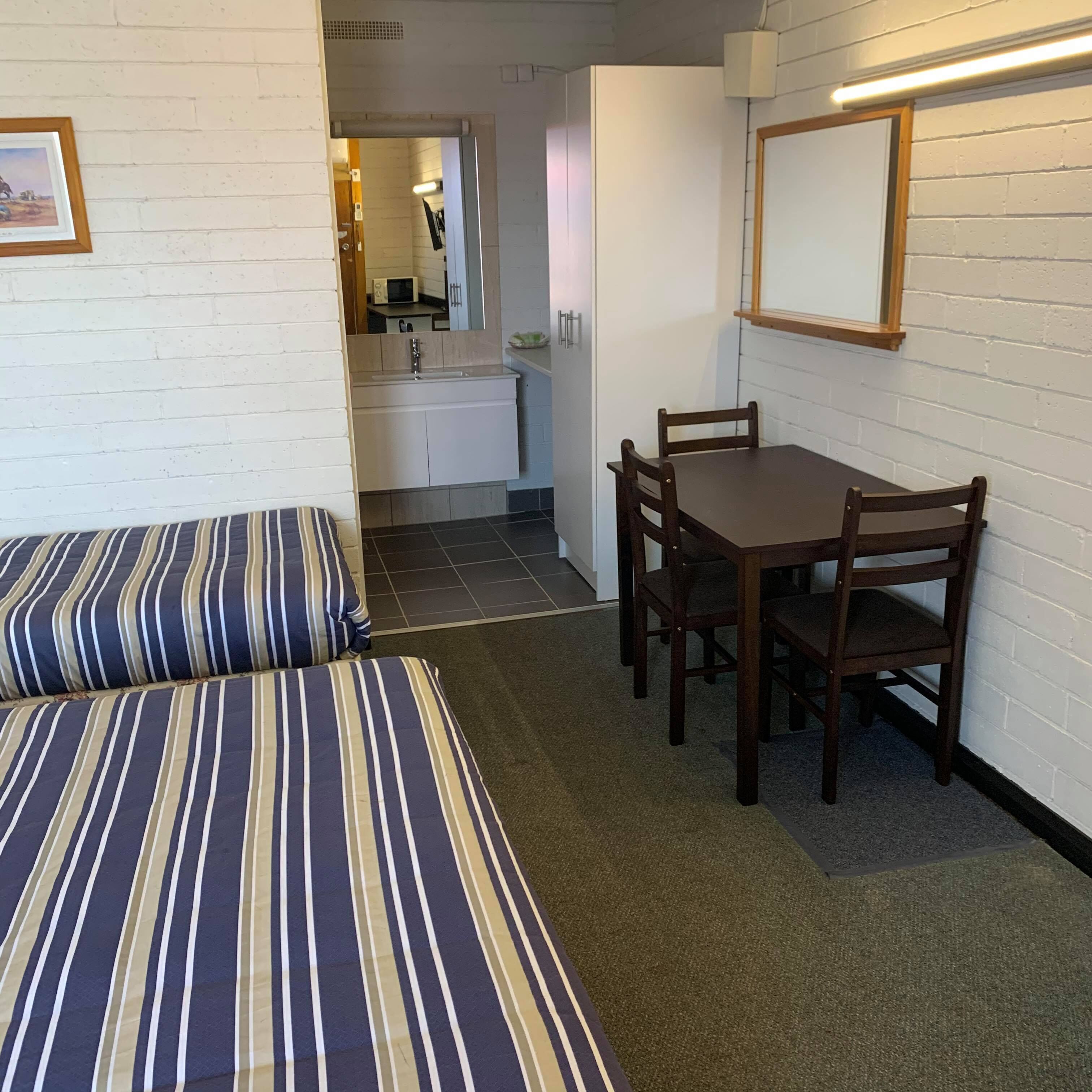 A compact room with a striped sofa, a wooden dining table with four chairs, and a small kitchenette in the background.