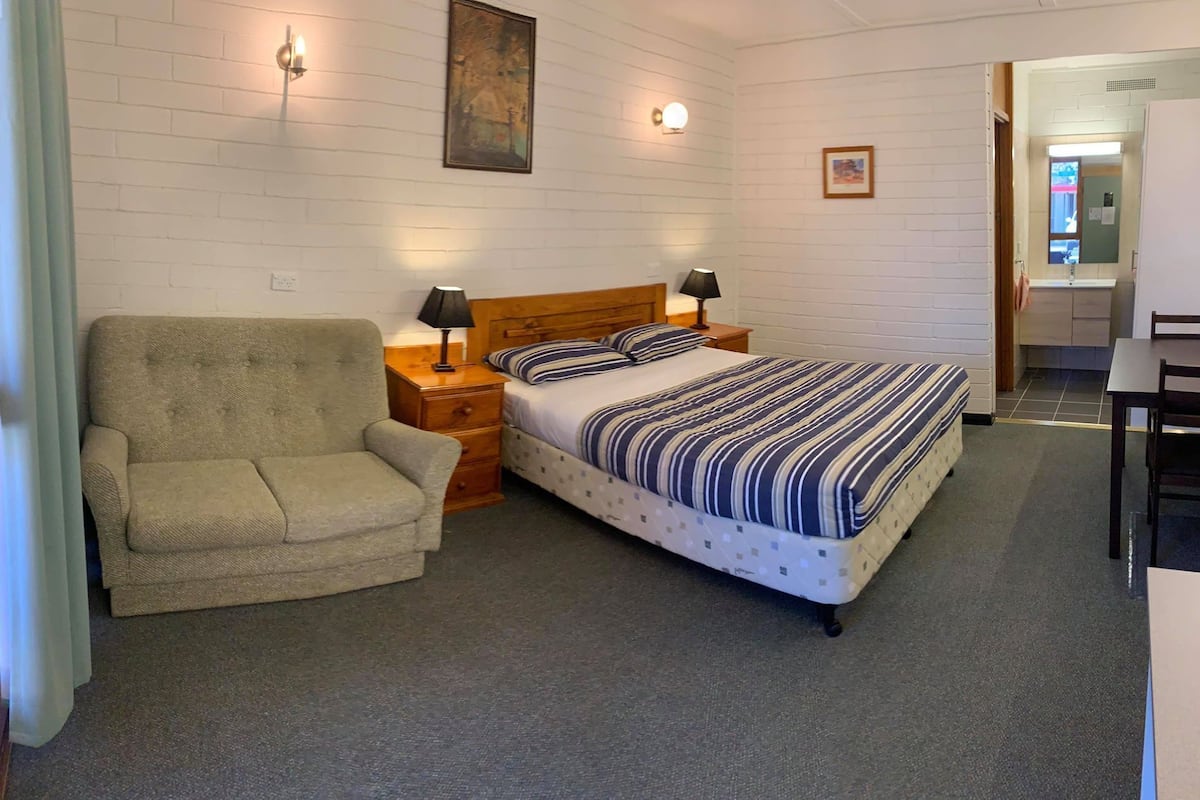 Une chambre à coucher avec un lit, une chaise, une table de chevet et une lampe.