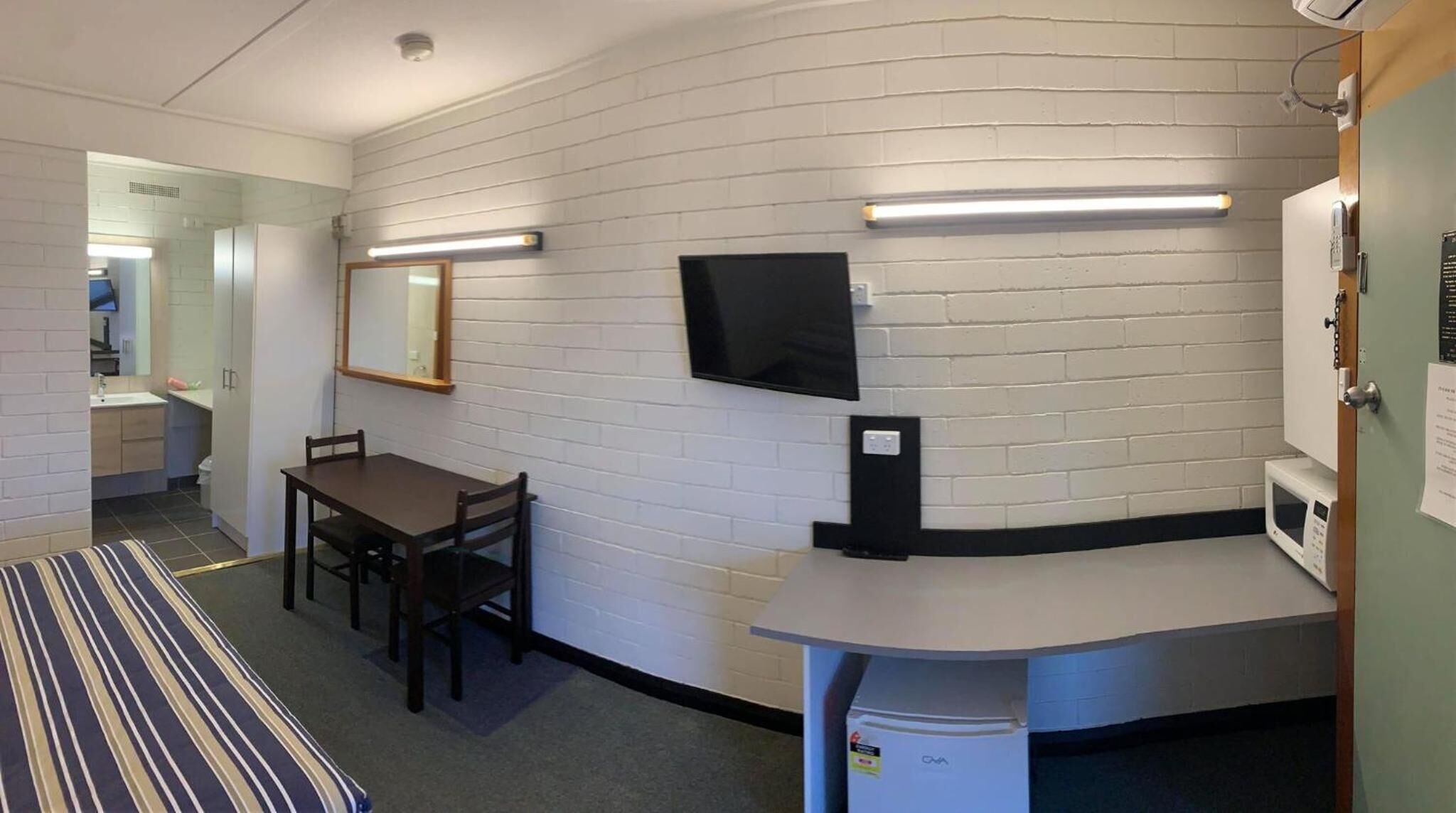 A compact room with a bed, a desk, a chair, a television, and a microwave.
