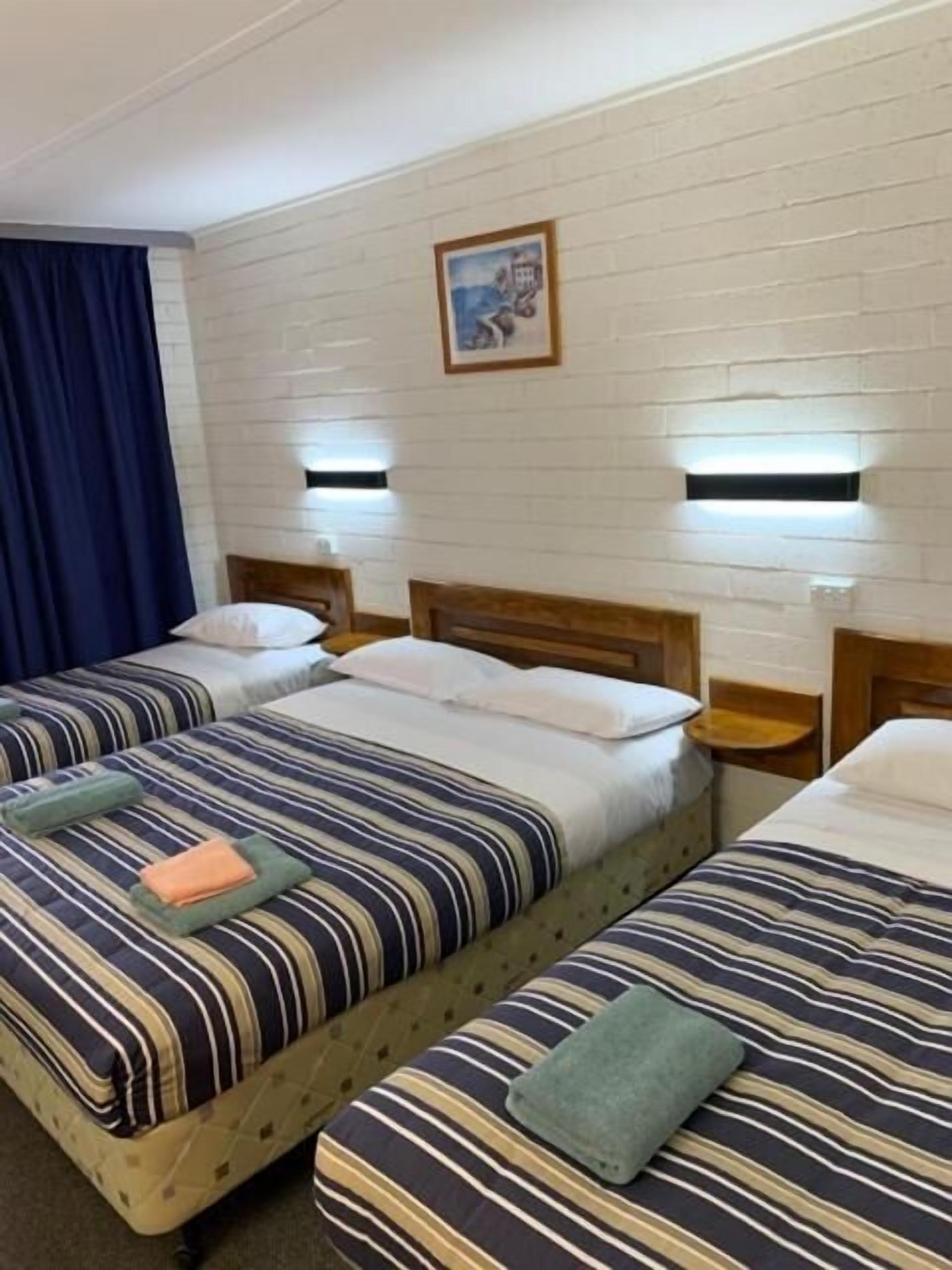 Ein Zimmer mit zwei Betten, jeweils mit gestreifter Bettwäsche und Kissen, einem Holzkopfstück und einer wandmontierten Lampe.