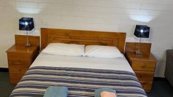 Een hotelkamer met een eenpersoonsbed, twee nachtkastjes met lampen, een lijst aan de muur en een klein houten nachtkastje.