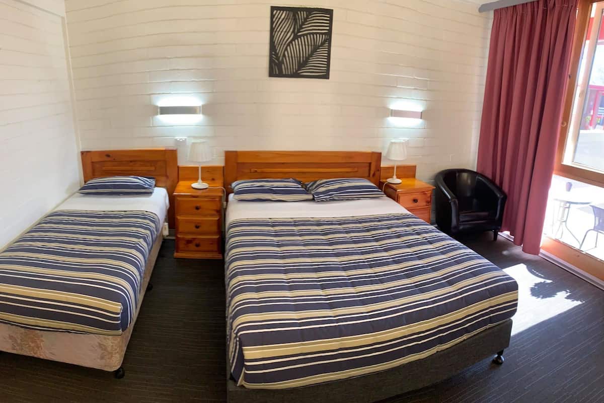Une chambre avec deux lits, chacun doté de draps à rayures, de têtes de lit en bois, de tables de chevet avec des lampes et d’un rideau rouge à la fenêtre.