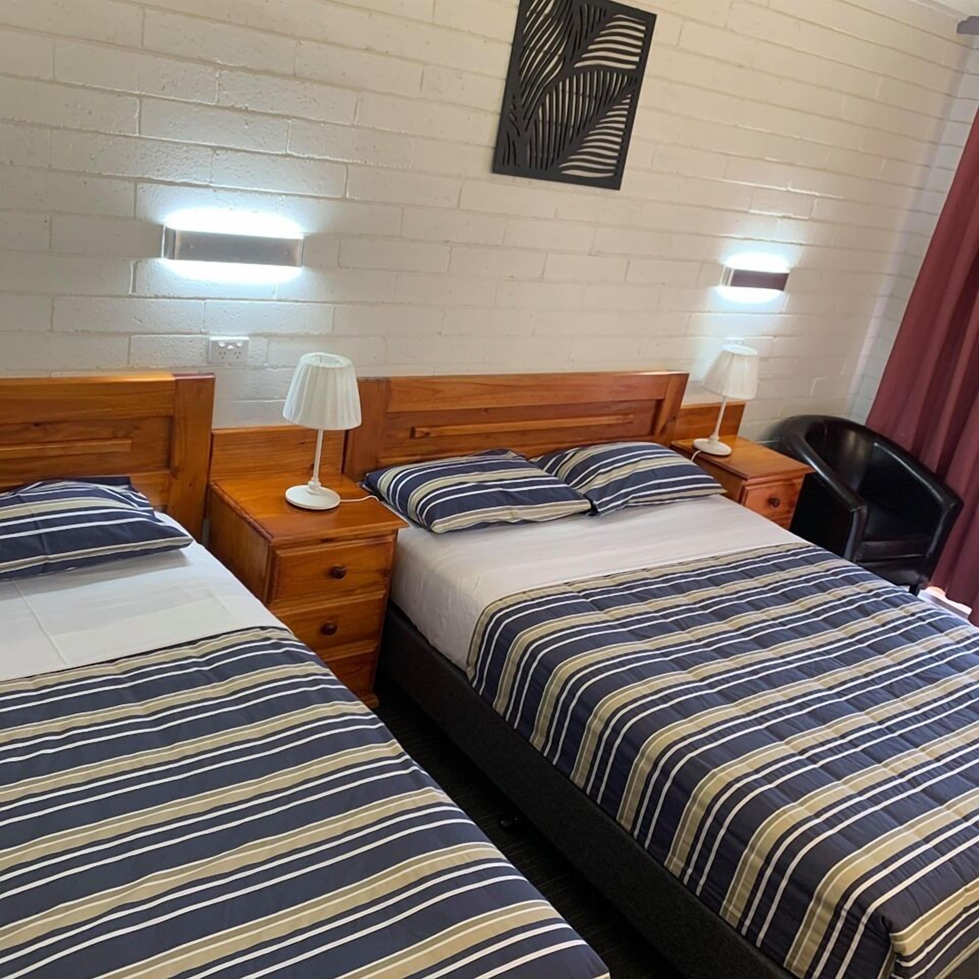 Ett hotellrum med två sängar, där varje säng har randiga sängkläder, trägavlar och sängbord med lampor.