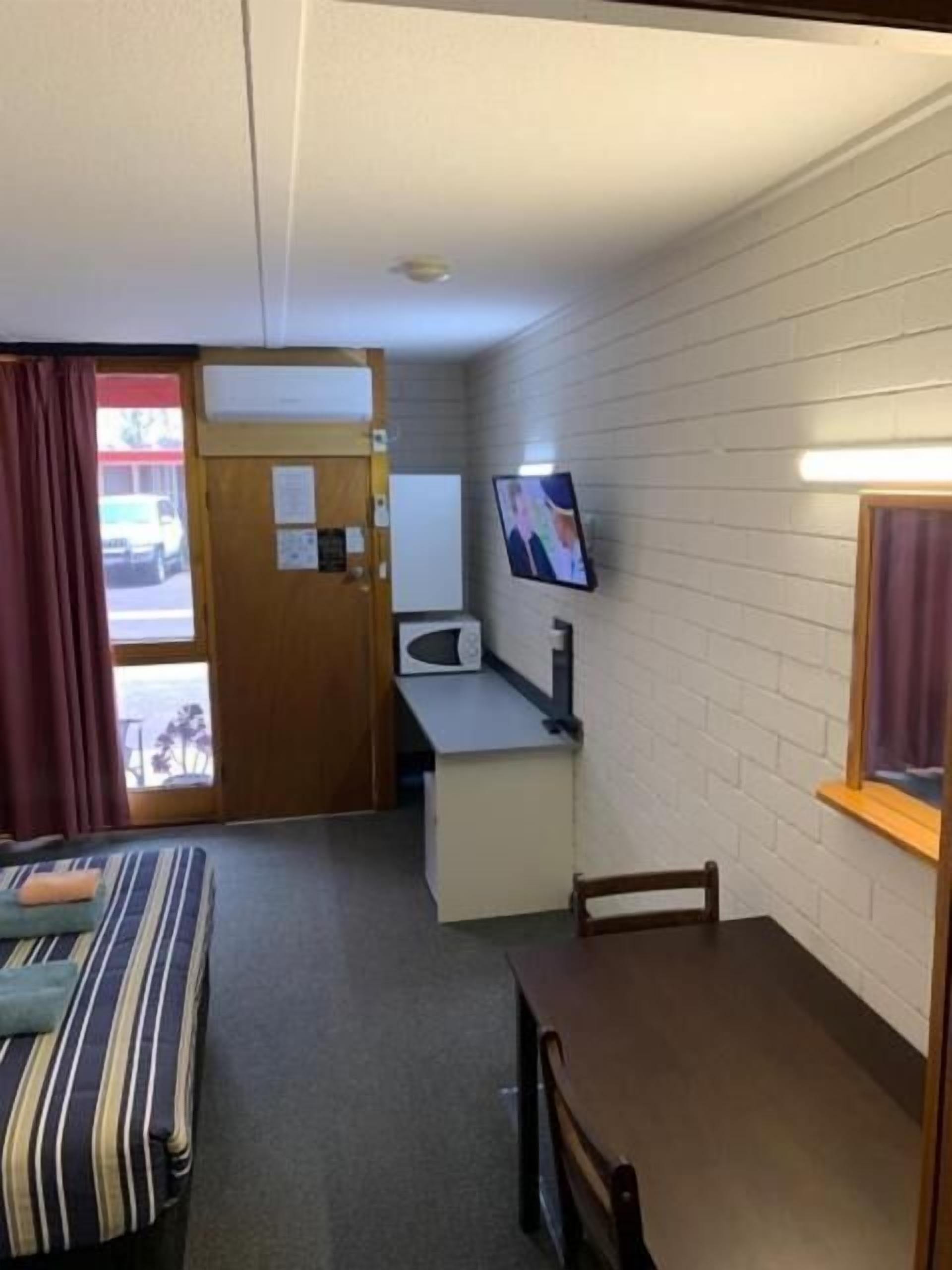 Une chambre d’hôtel compacte comprenant un lit, une petite table à manger, un téléviseur fixé au mur et un coin cuisine.