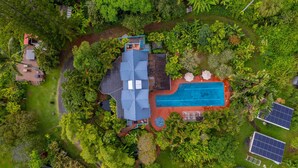 Vista aérea de una propiedad con piscina, paneles solares y exuberante vegetación.
