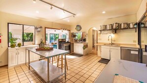 Una cocina amplia con una isla central, muebles blancos y vistas a un balcón.