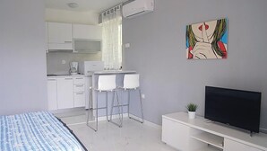 A modern bedroom with a bed, a TV, a desk with two chairs, a kitchenette, and a painting on the wall. - Nice studio in Rabac with house sea view (Rabac)