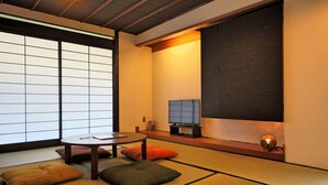 A traditional Japanese room with tatami flooring, a low table, cushions, a television, and a sliding door. - Setouchi Mangetsusou (Takamatsu)