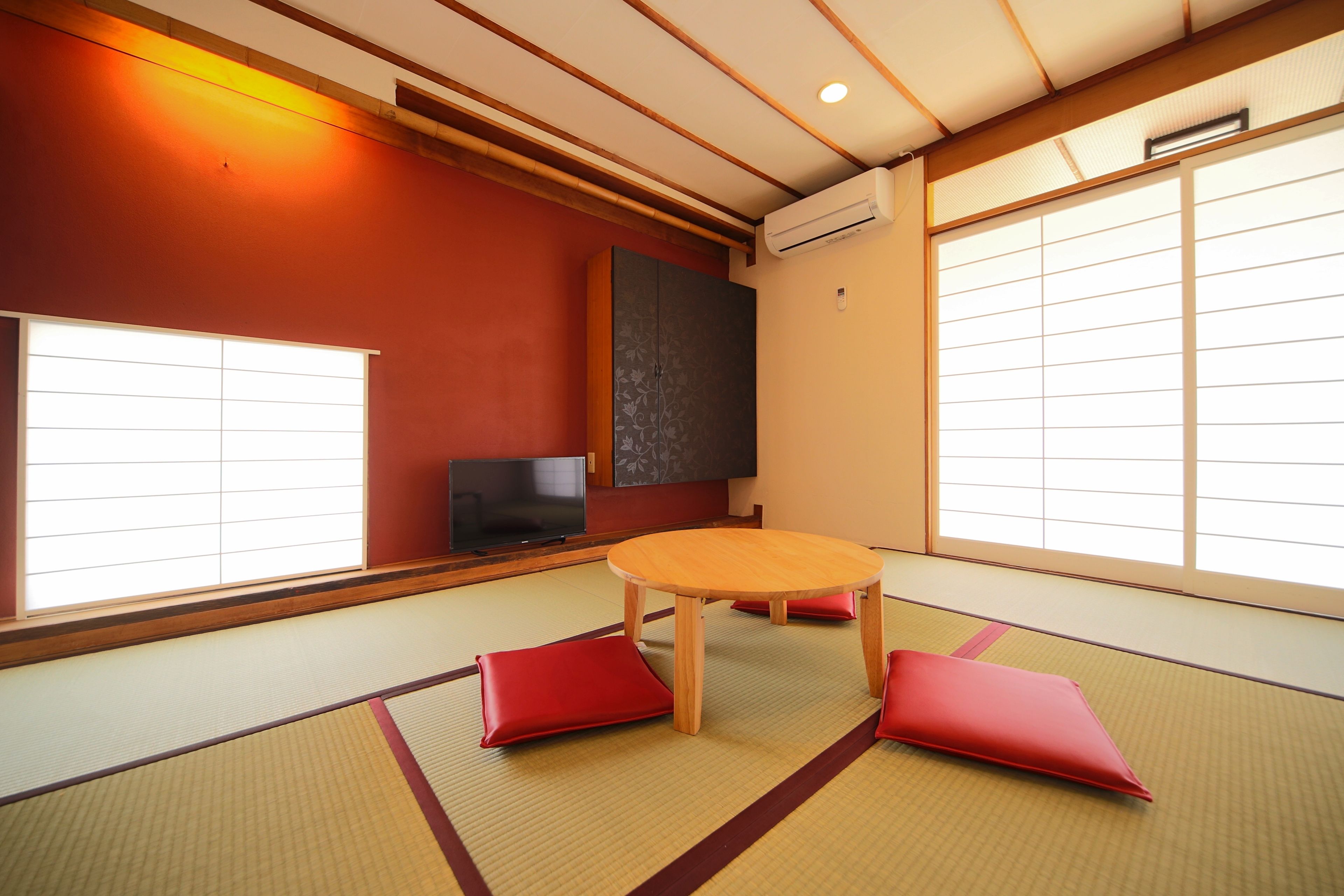 Una habitación japonesa tradicional con suelo de tatami, una mesa de madera baja y cojines rojos.