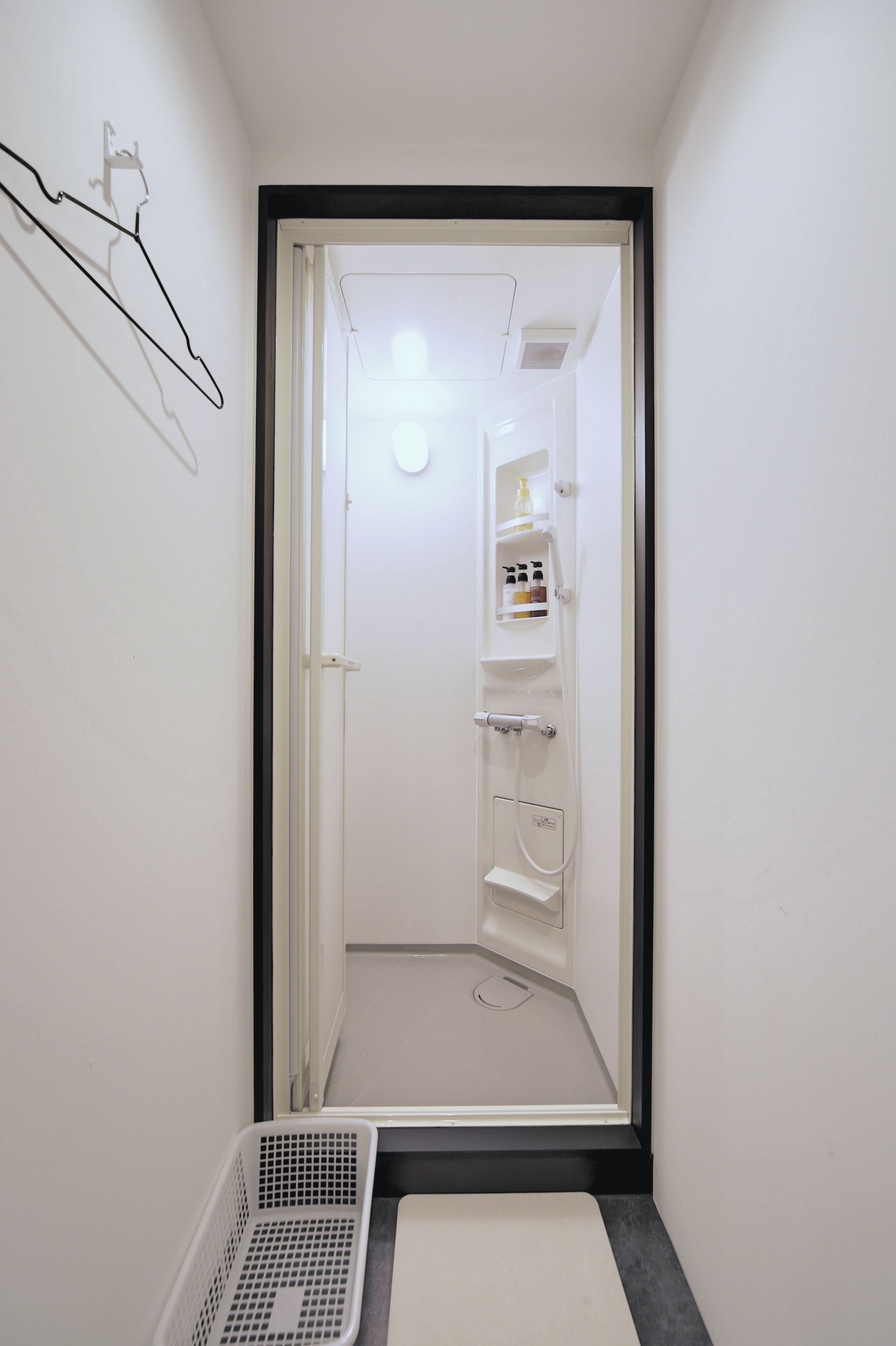 Un corridoio stretto che conduce al bagno, dove si trova una doccia, un porta asciugamani e un piccolo ripiano con articoli da toilette.