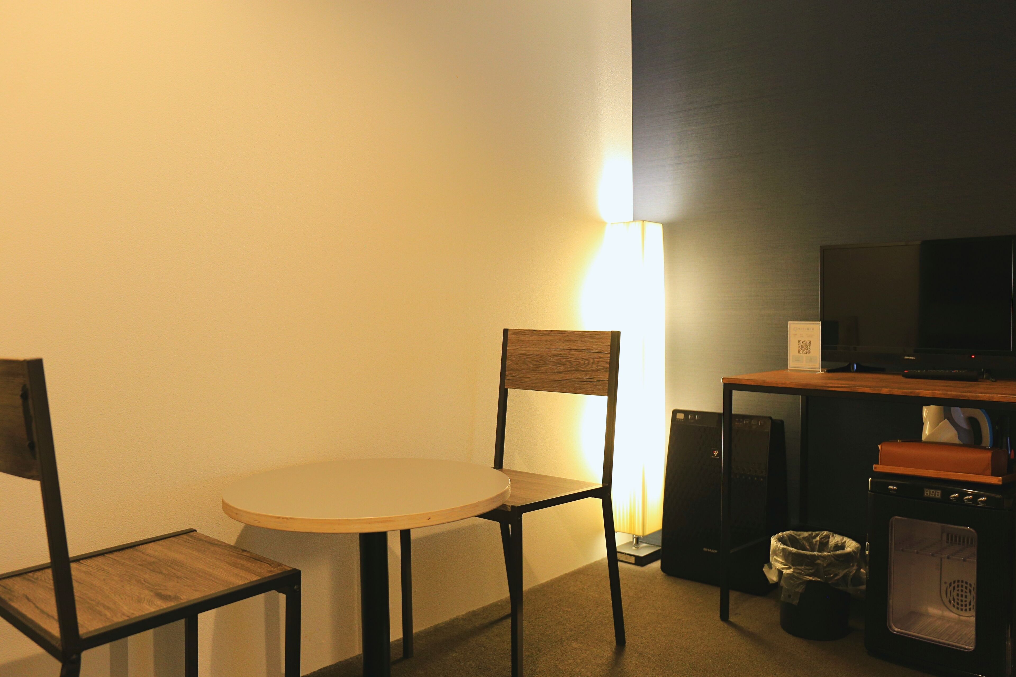 A small room with a round table, two chairs, a television, a heater, and a trash bin.
