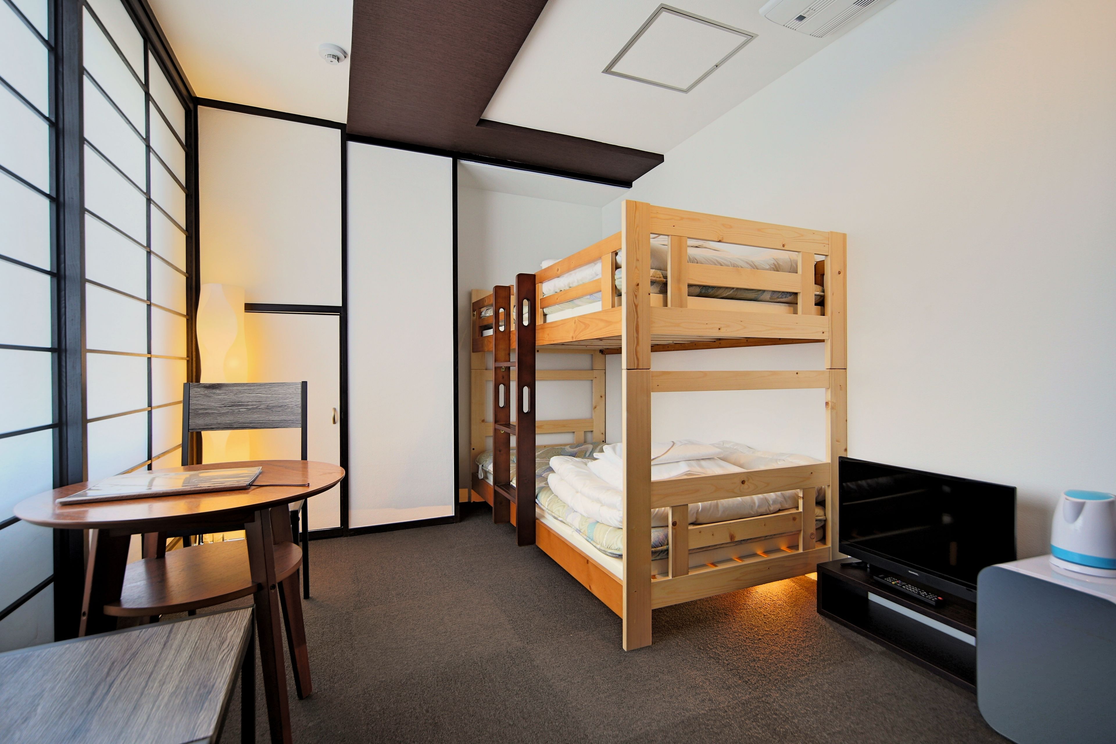 A compact hotel room with a bunk bed, a small table with chairs, a lamp, and a television.
