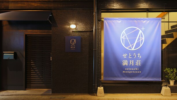 A building facade with a dark wooden exterior, a blue banner with white text, and a small sign with Japanese characters. - Setouchi Mangetsusou (Takamatsu)