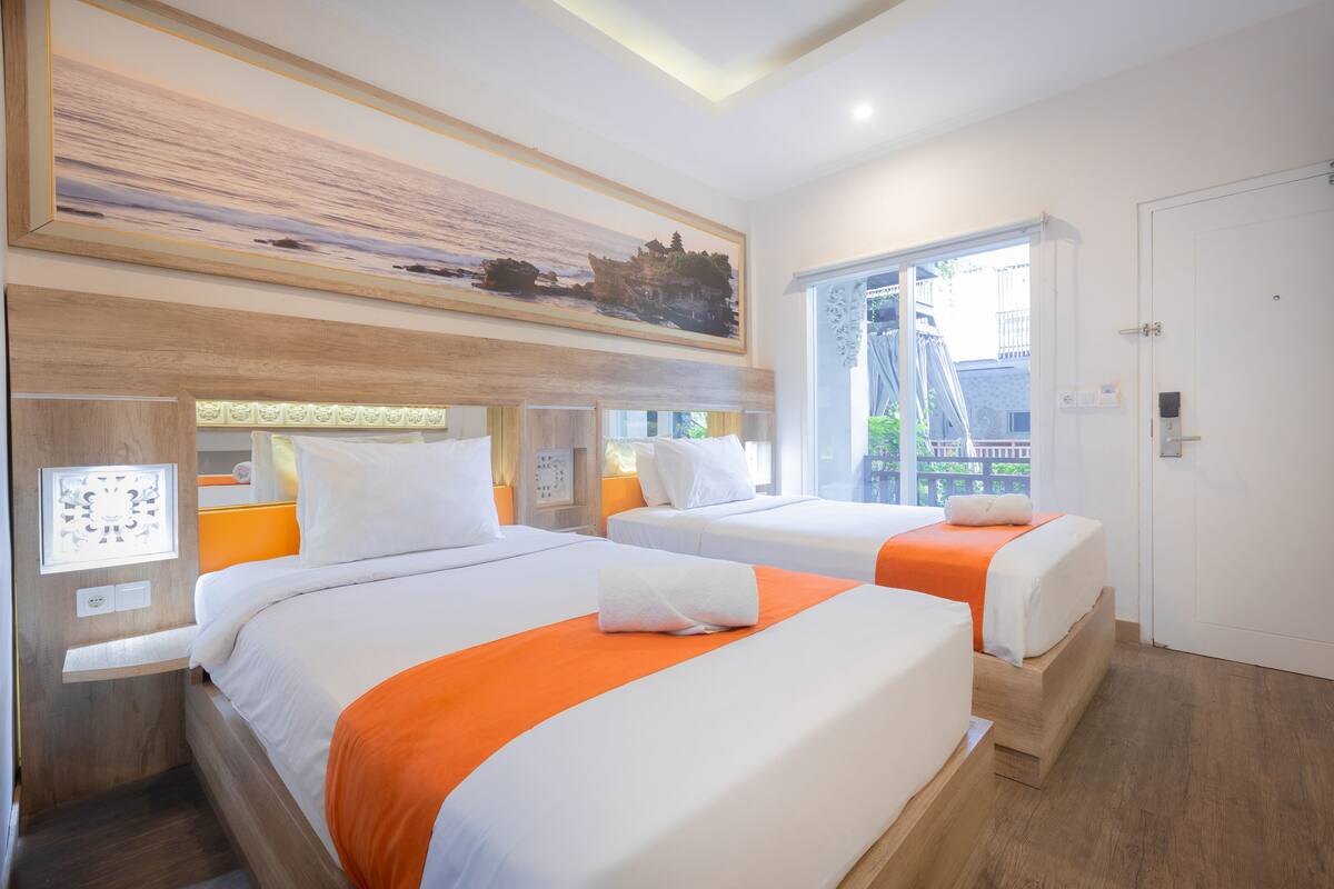 A hotel room with two beds, a large window, and a painting on the wall.