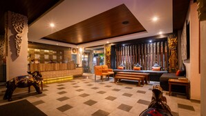 Un vestíbulo amplio con suelo a cuadros, una recepción, zona de estar con sofá y sillones, y estatuas decorativas.