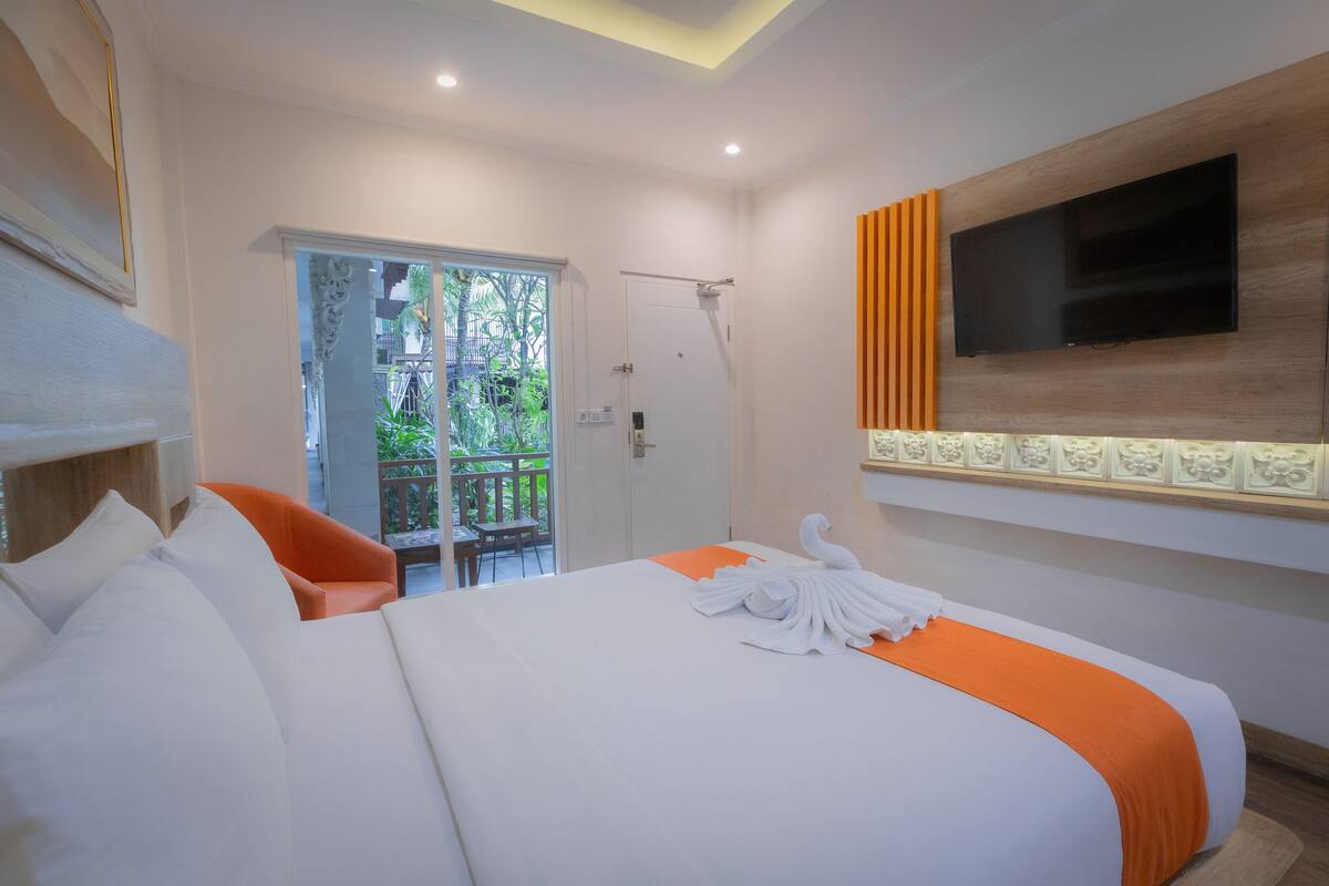 A hotel room with a large bed, a TV mounted on the wall, and a balcony with a view of greenery.