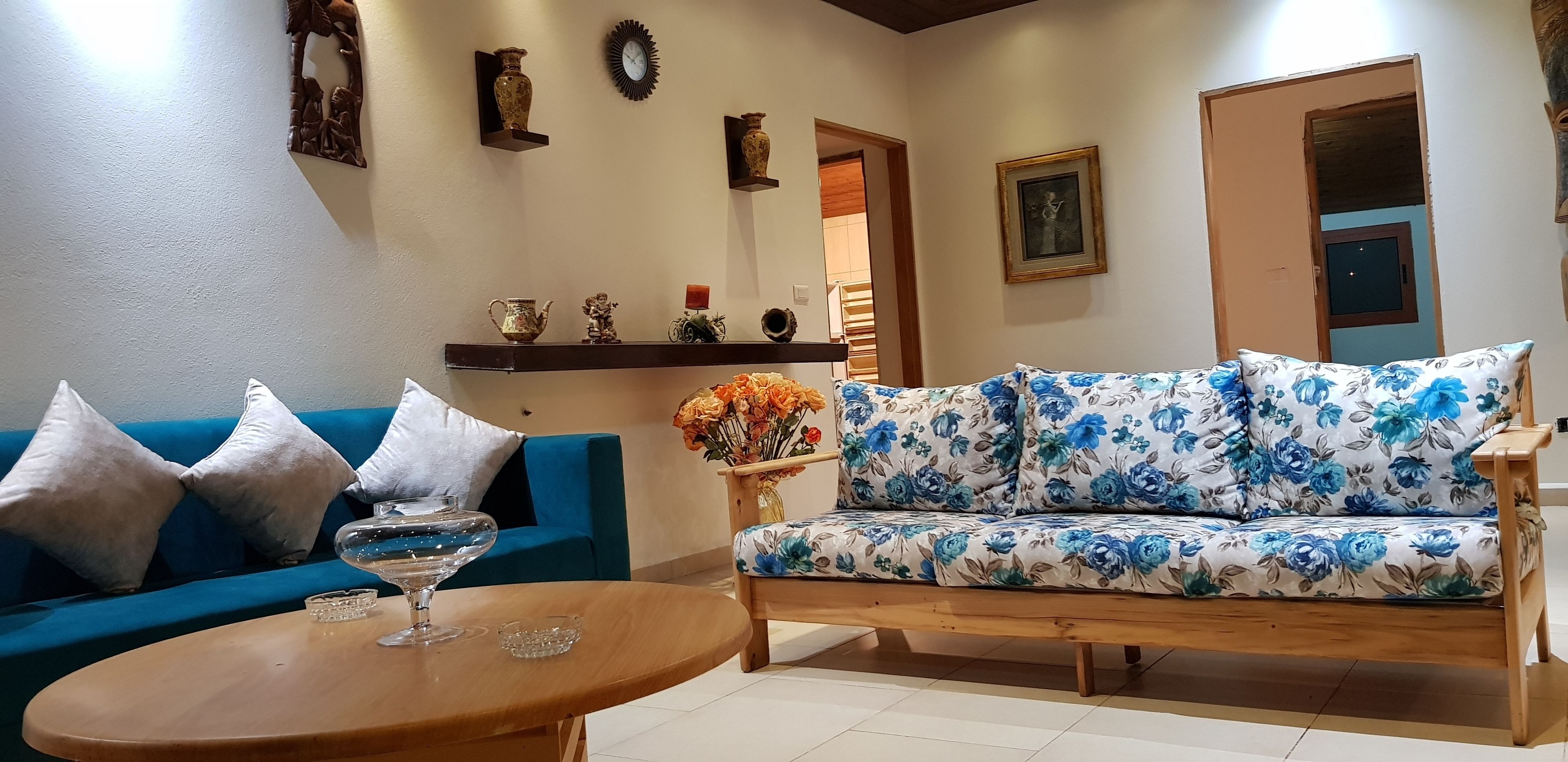 A living room with a blue sofa, a floral sofa, a wooden coffee table, and decorative items on shelves.