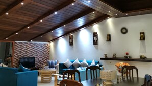 A spacious living area with a high ceiling, wooden beams, and recessed lighting. There is a blue sofa, a dining table with chairs, and a television on a wall. - Apartment near Lady of the Sea & Phoenician Wall (Batroun)