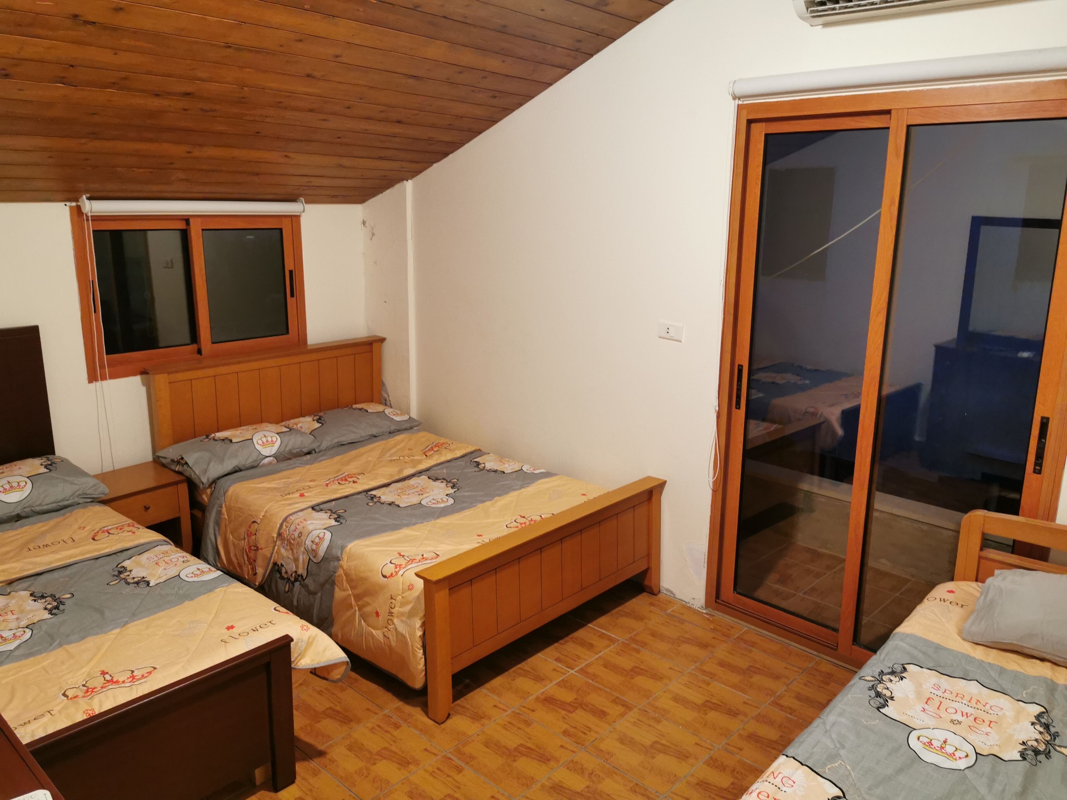 Un dormitorio con dos camas de madera, un ventanal corredero y techo de madera.