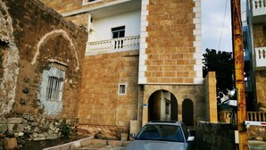 A silver car parked in front of a building with a stone facade, a balcony, and a small window with bars. - Apartment near Lady of the Sea & Phoenician Wall (Batroun)