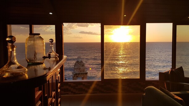 A room with a large window overlooking the sea, a wooden cabinet with glassware, and a stone lantern. - Apartment near Lady of the Sea & Phoenician Wall (Batroun)