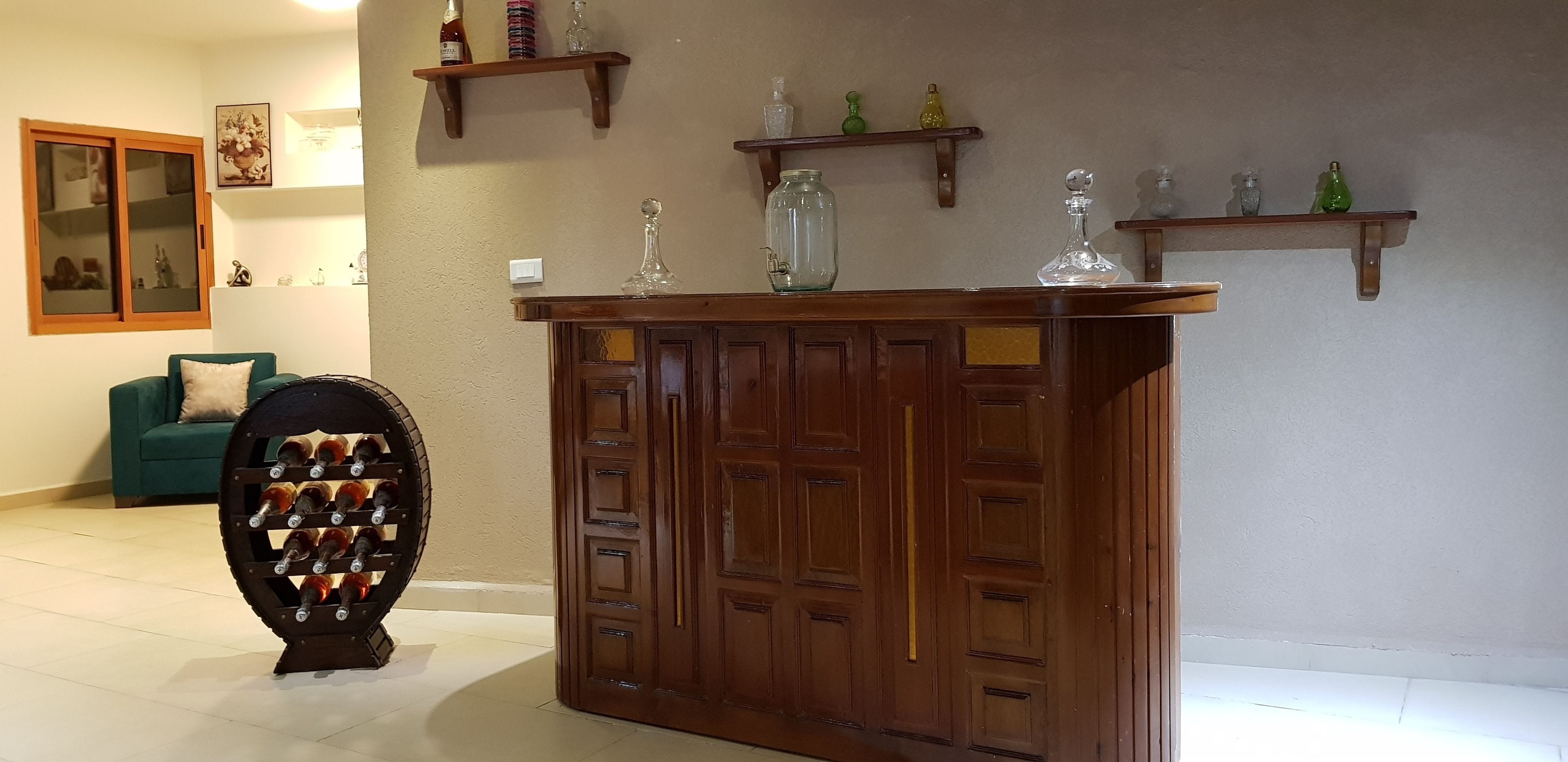 Una zona de bar de madera con un botellero, un sofá verde y estanterías decorativas.