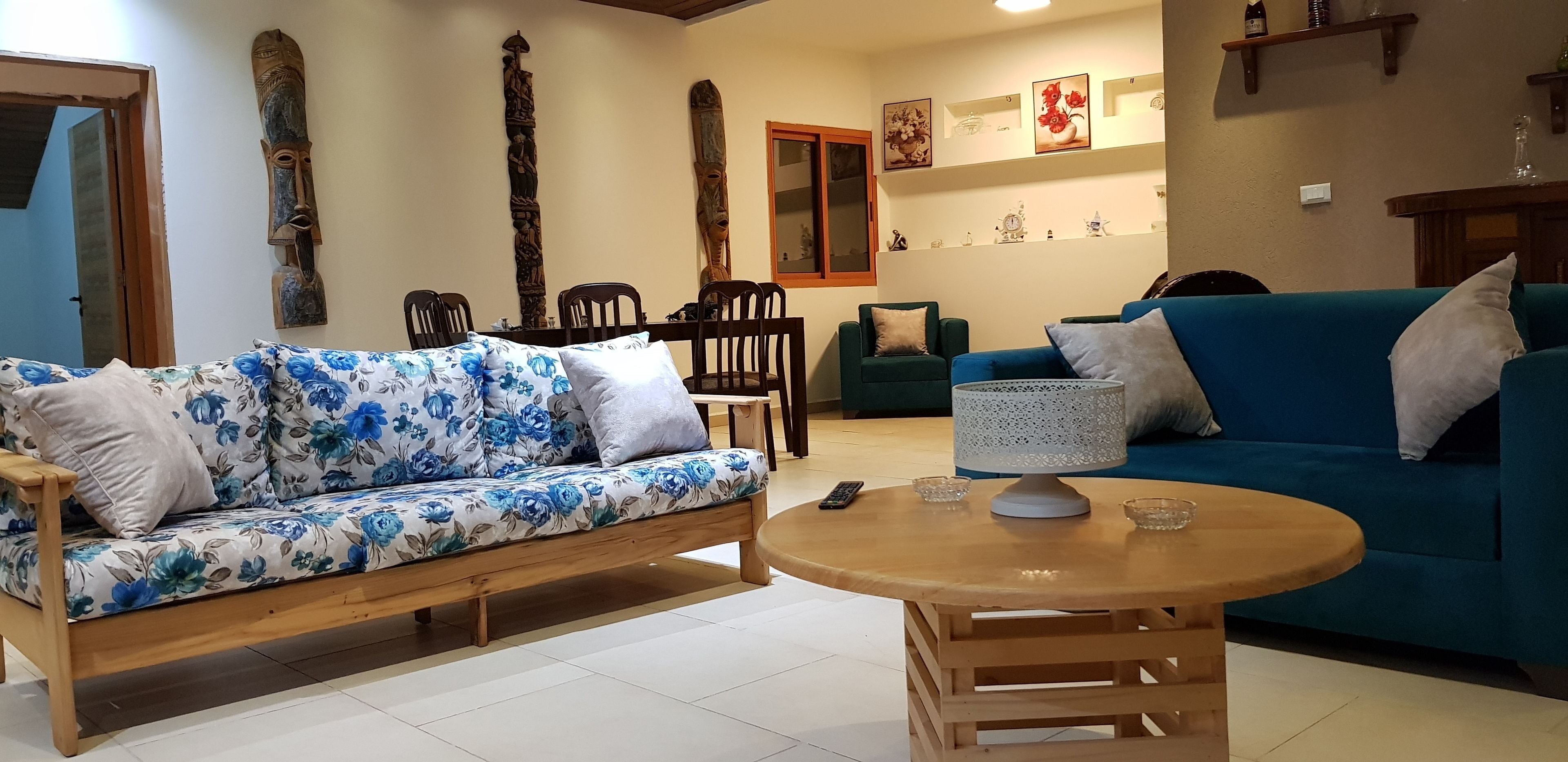 A living room with a floral sofa, a blue couch, a wooden coffee table, and a wall decorated with wooden carvings and framed pictures.