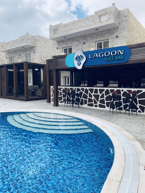 Un edificio moderno con un bar Lagoon Juice Bar, una piscina con un diseño único de mosaico azul y asientos al aire libre.