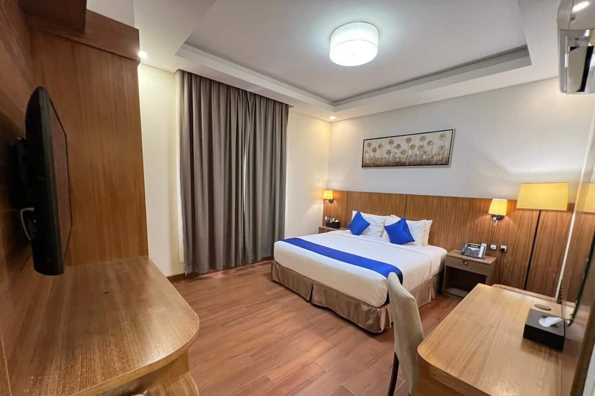 Habitación de hotel con cama, mesitas de noche, escritorio, silla, televisor y un cuadro en la pared.
