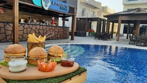 Zona de comedor junto a la piscina, con hamburguesas, papas fritas y salsas.