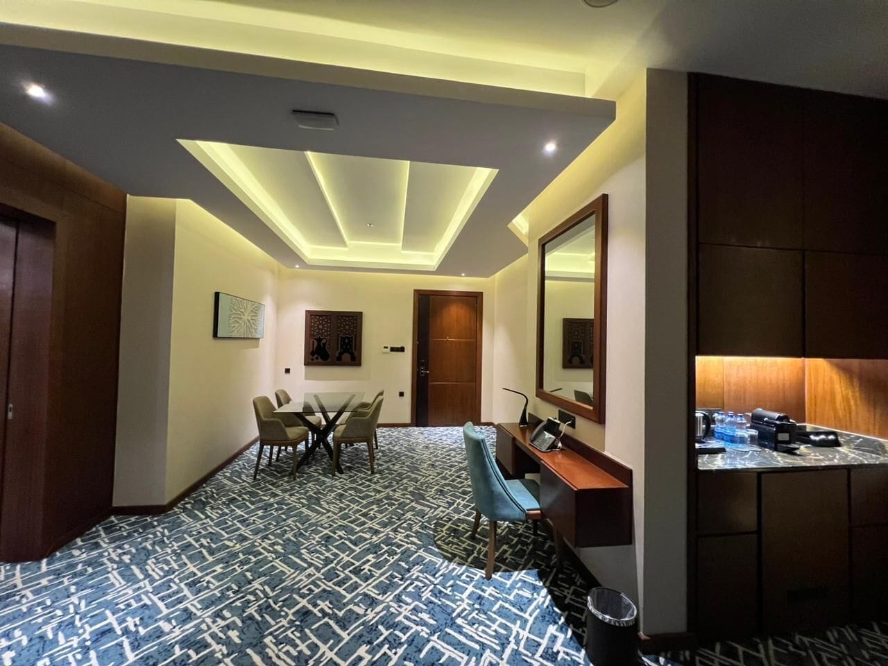 Habitación de hotel con comedor, un escritorio con silla, un espejo grande y un minibar.
