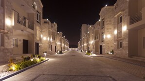 Vista nocturna de una calle residencial con casas uniformes, ventanas iluminadas y una carretera pavimentada.