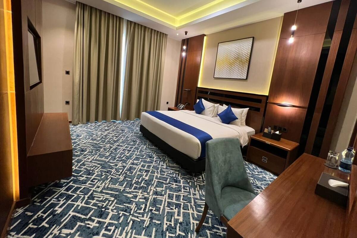 Habitación de hotel con una cama grande, un escritorio, una silla, una mesita de noche y una obra de arte colgada en la pared.
