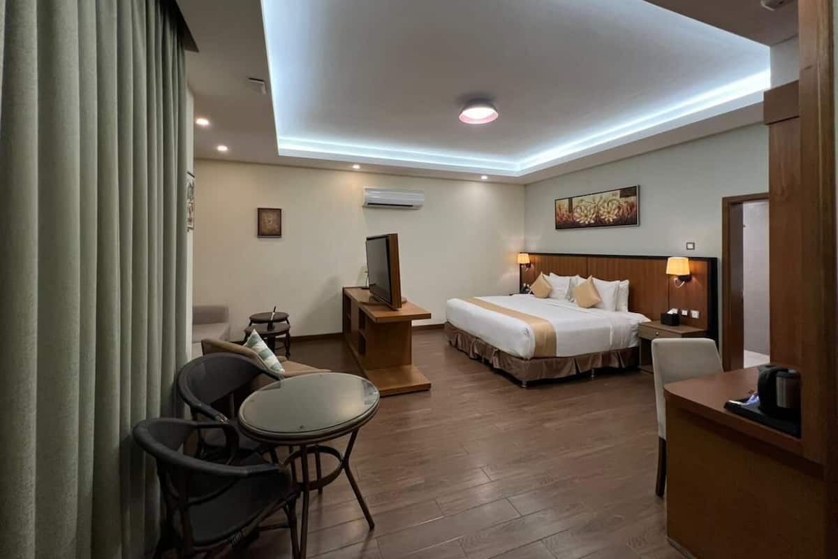 Una habitación de hotel con cama, mesitas de noche, televisor, escritorio y silla.