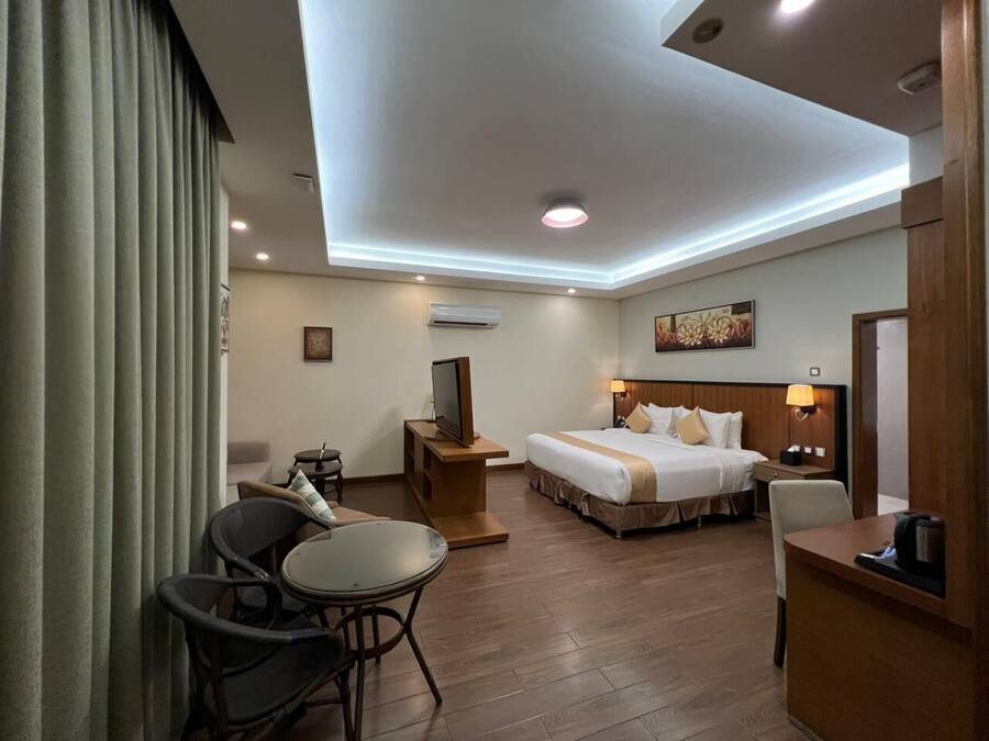 Quarto de hotel com cama, mesas de cabeceira, televisão, escrivaninha e cadeira.