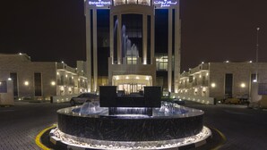 Un hotel moderno con una fuente central, señalización iluminada y una entrada bien iluminada.