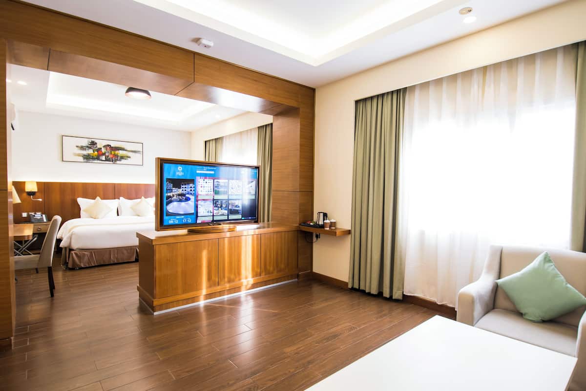 Una habitación de hotel con escritorio de madera, televisor de pantalla plana, cama, sofá y una ventana grande con cortinas.