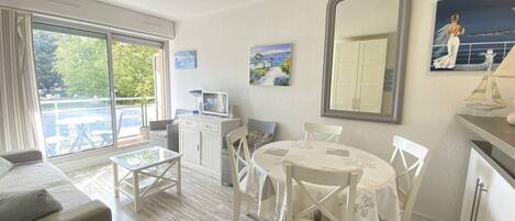 Una habitación con balcón, una mesa de comedor con sillas, un sofá, un televisor y un espejo grande.