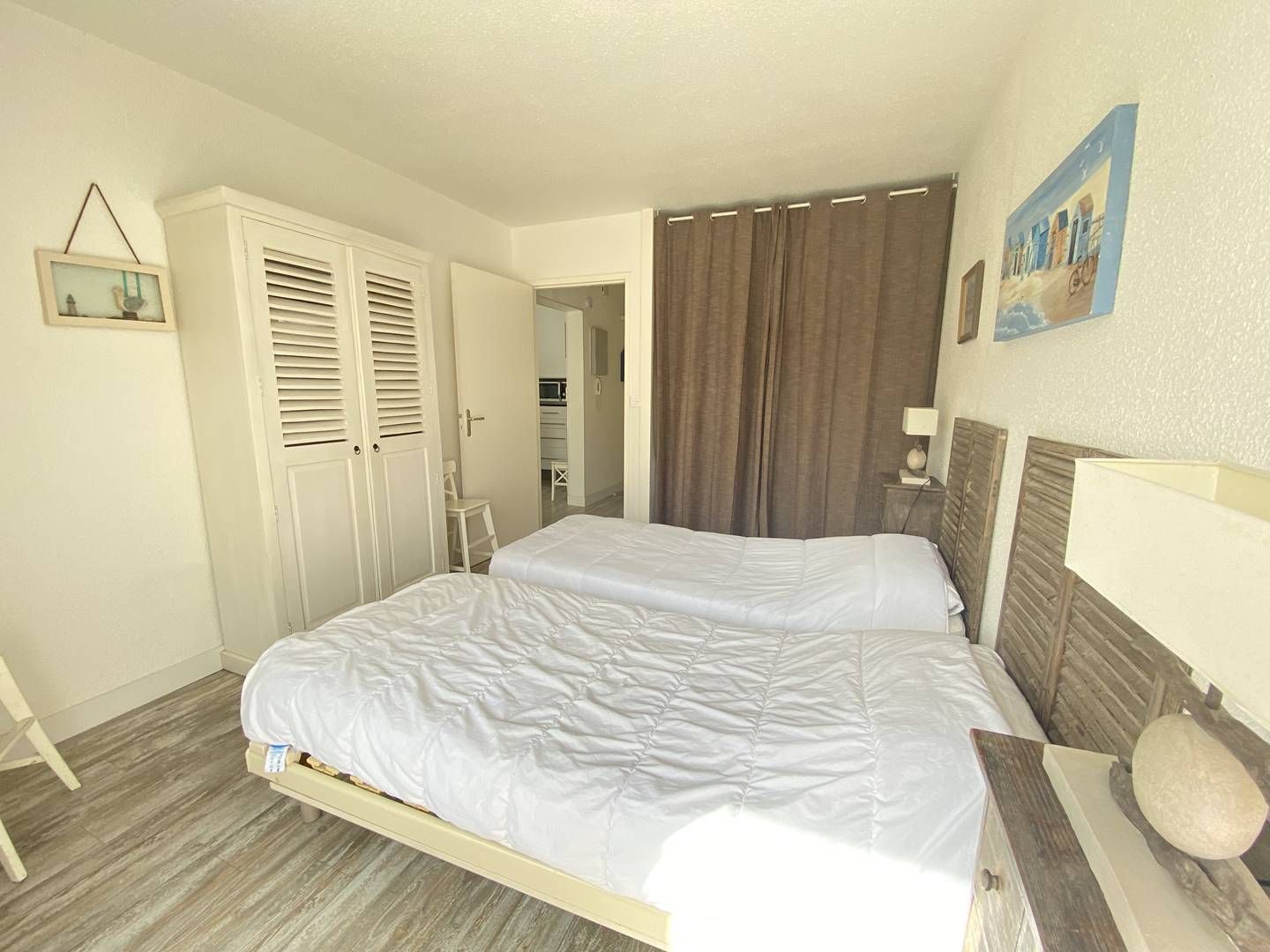 A bedroom with two beds, a wardrobe, a mirror, and a painting on the wall.