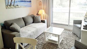 A living room with a sofa, a coffee table, a chair, and a large window with a view of the outdoors. - Beautiful 2 rooms Moulleau center with parking (ARCACHON)