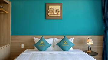 A hotel room with teal walls, a bed with white bedding, two teal pillows, a framed picture on the wall, and a nightstand with a lamp.