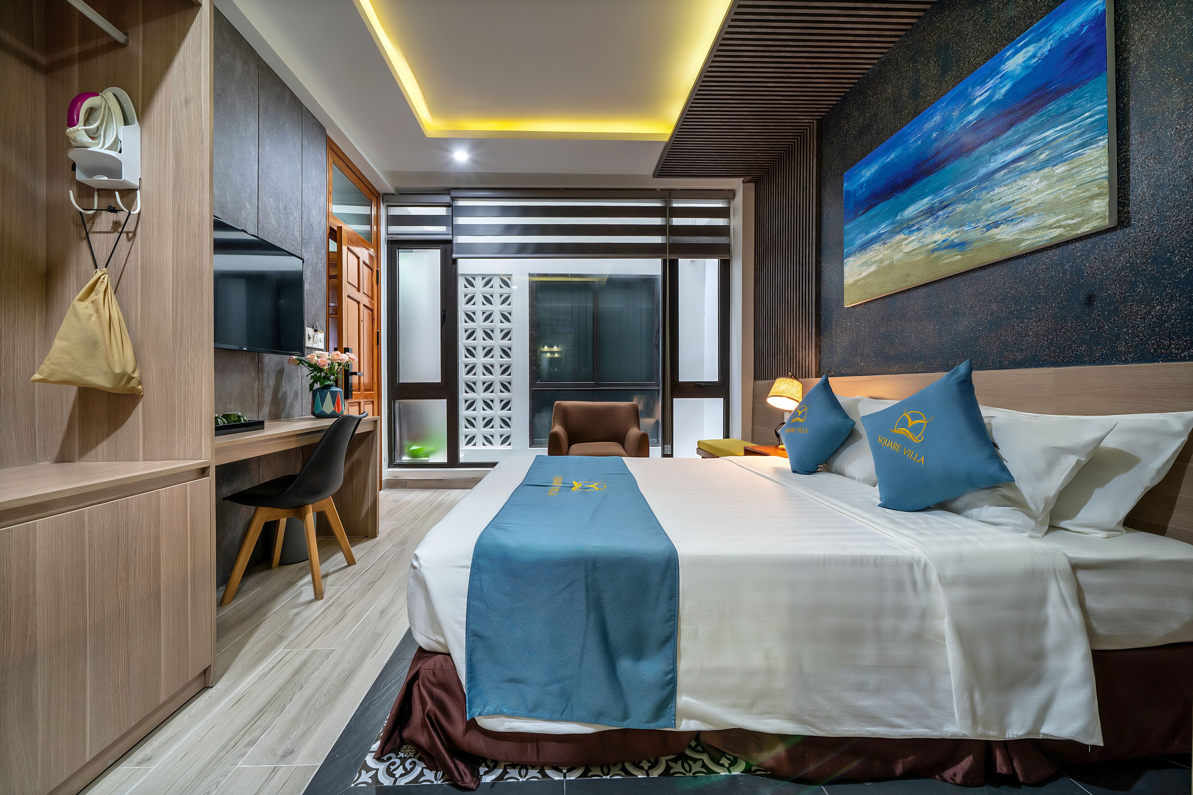 A hotel room with a bed, desk, chair, and a view of the outside.