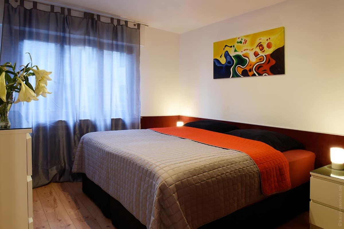 Ein Schlafzimmer mit Bett, Vorhängen, einem Gemälde und einem Nachttisch mit Lampe.