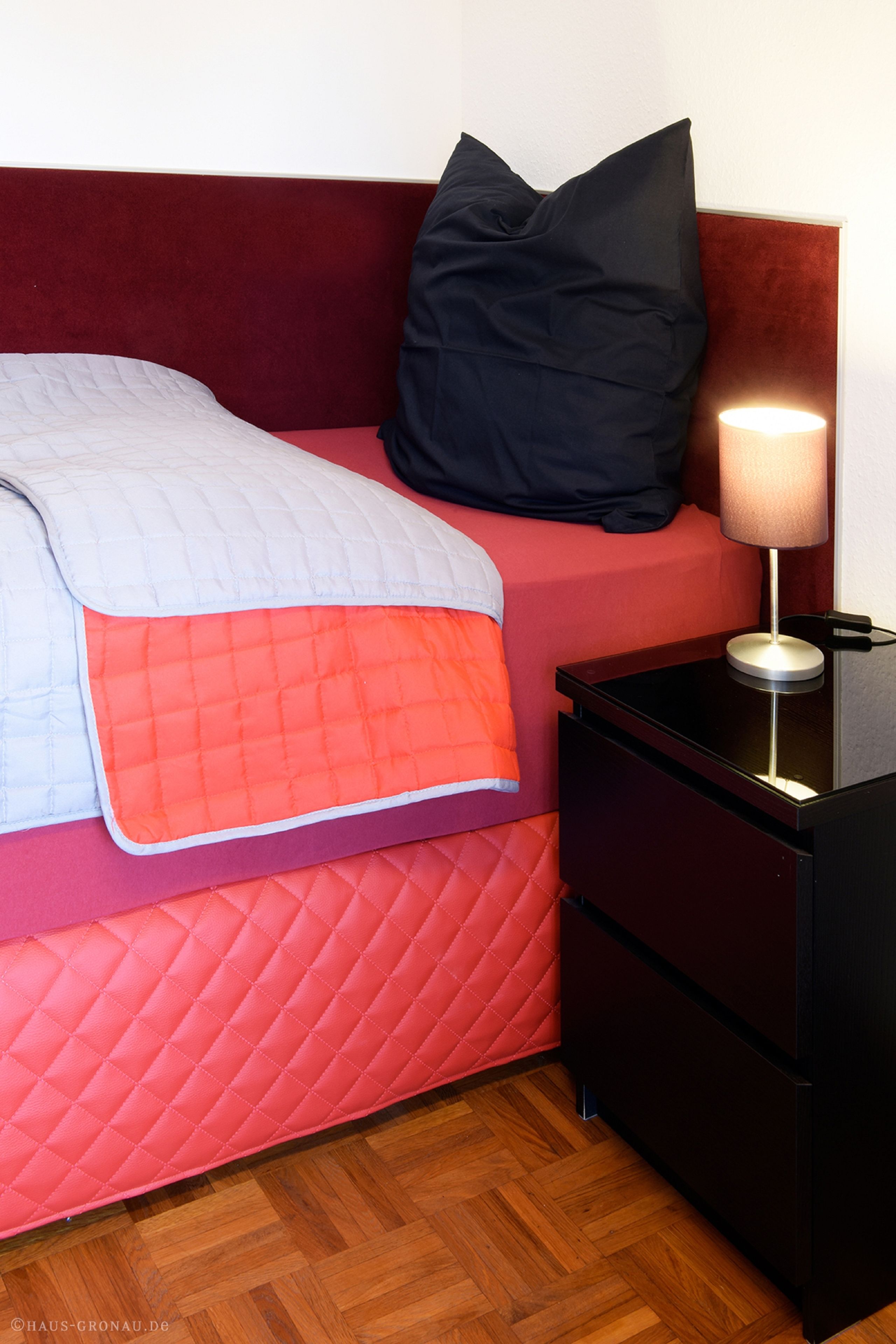 Ein Bett mit gesteppter Bettdecke, ein Nachttisch mit Lampe und ein Holzboden.