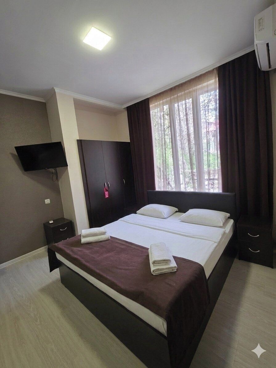 A bedroom with a bed, a flat-screen TV, a wardrobe, a nightstand, and an air conditioning unit.