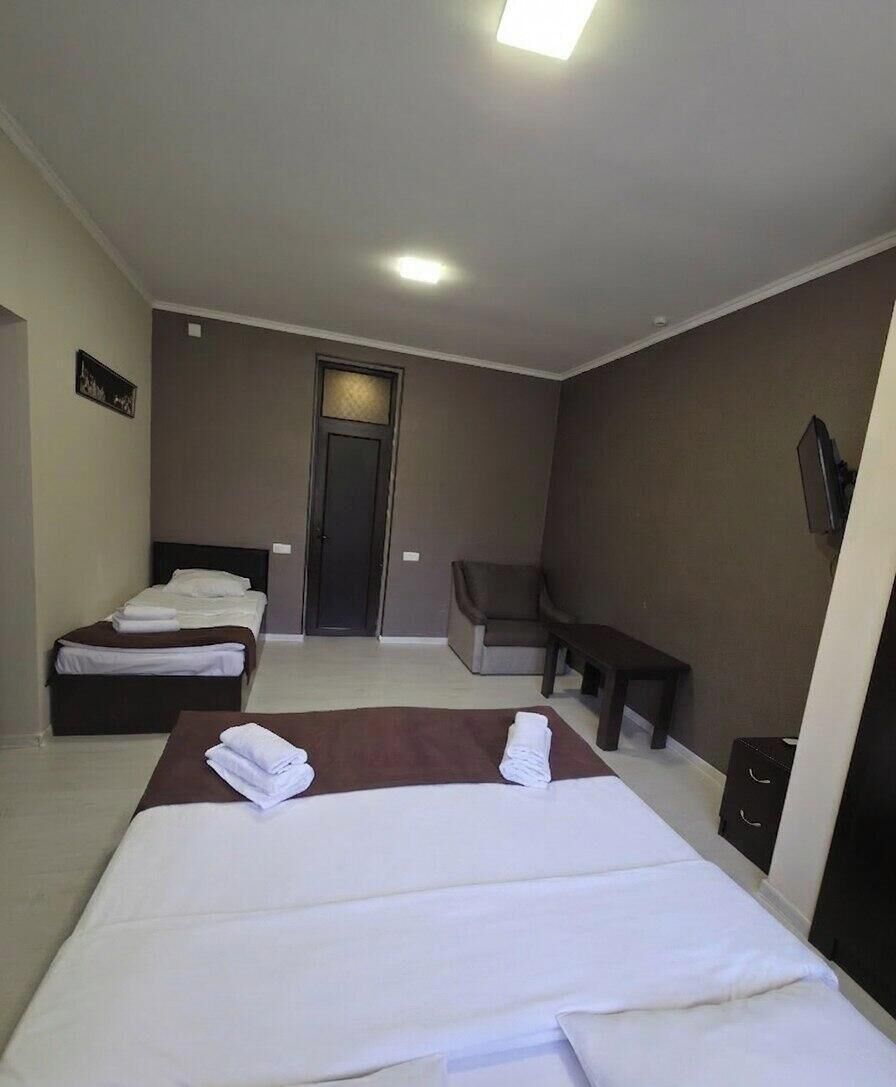 A hotel room with two beds, a sofa, a bench, and a TV.