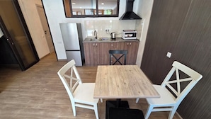 Una cocina compacta con una mesa de madera y sillas blancas, un refrigerador y un microondas.