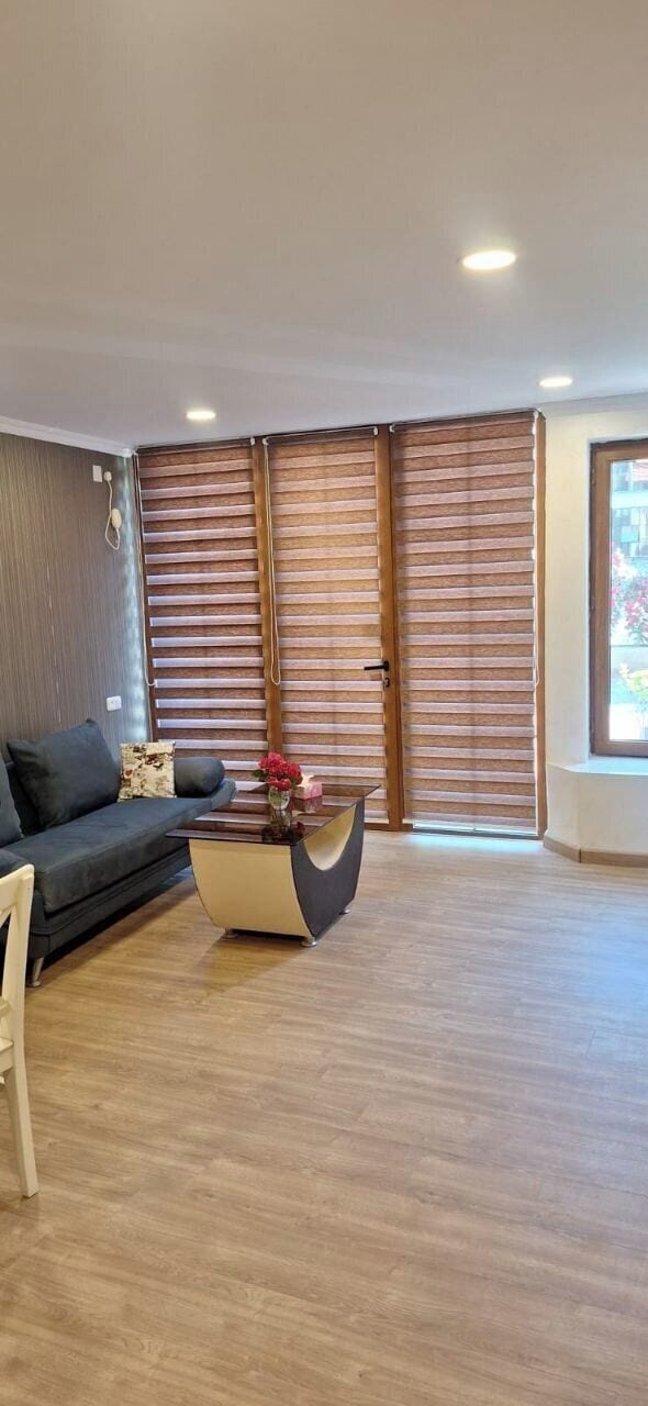 A modern living room with a sofa, a coffee table, and a window with blinds.